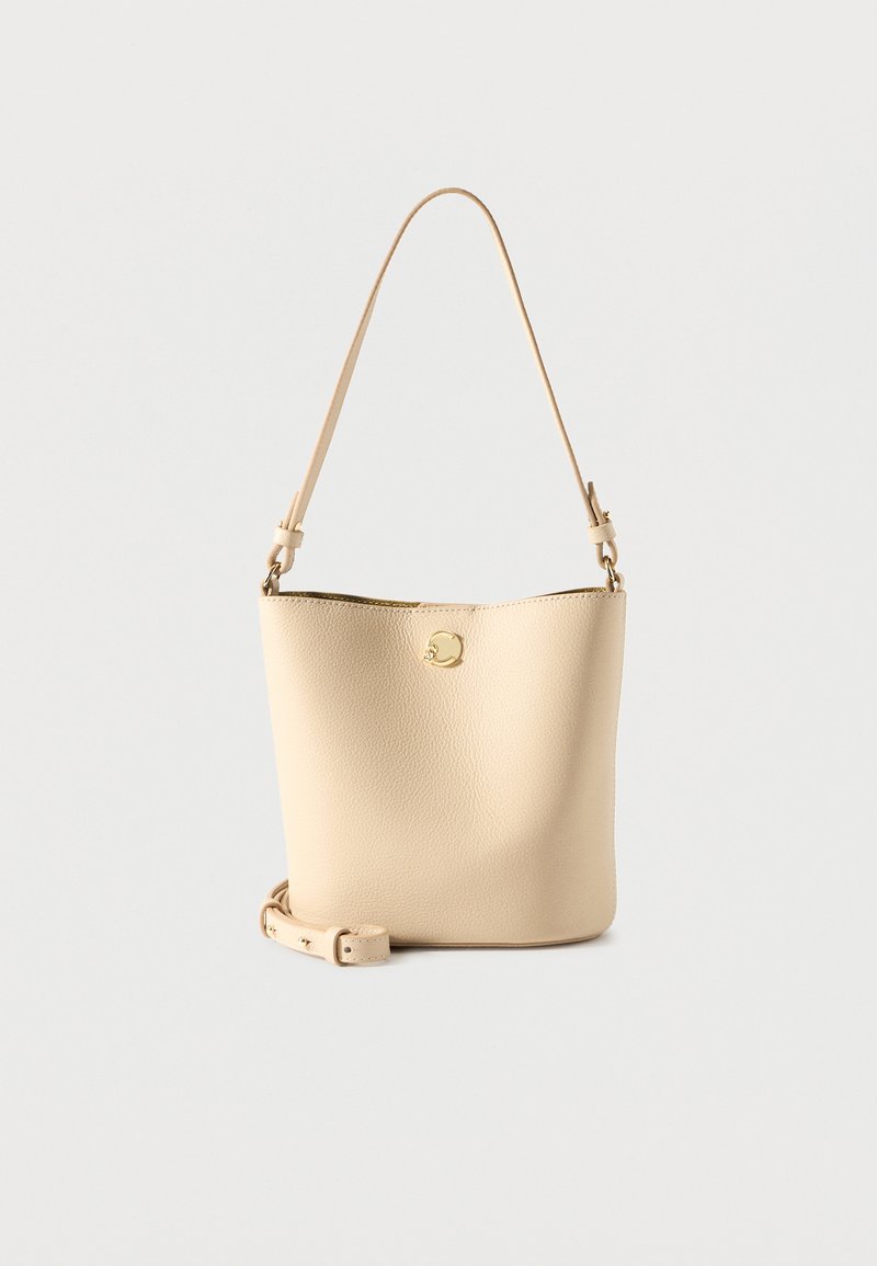 Τσάντα κάδου από μπεζ δέρμα με λαβή στο επάνω μέρος και αποσπώμενο ιμάντα ώμου, που διαθέτει μικρό χρυσό κυκλικό λογότυπο σε απλό φόντο.