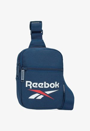 Pequeña bolsa bandolera Reebok azul marino con logo blanco y rojo, bolsillo frontal con cremallera y correa ajustable.
