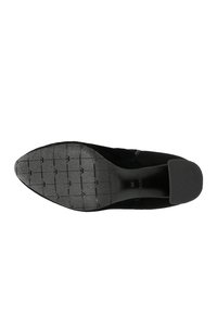 Černá semišová bota s špičatou špičkou, texturovanou gumovou podrážkou s mřížkovým vzorem a plochým podpatkem. Minimalistický design bez dekorací.