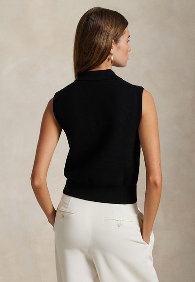 Melns adīts bezroku tops ar apkakli, ribota tekstūra, pieguloša vidukļa daļa un gluda apdare, kombinēts ar krēmkrāsas biksēm ar aizmugurējām kabatām.