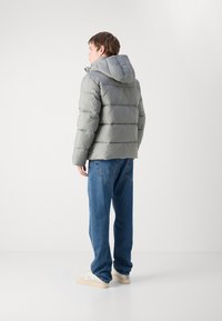Polstret grå jakke med hætte, med en quiltet design og en afslappet pasform, parret med blå denim jeans og lyse sneakers.