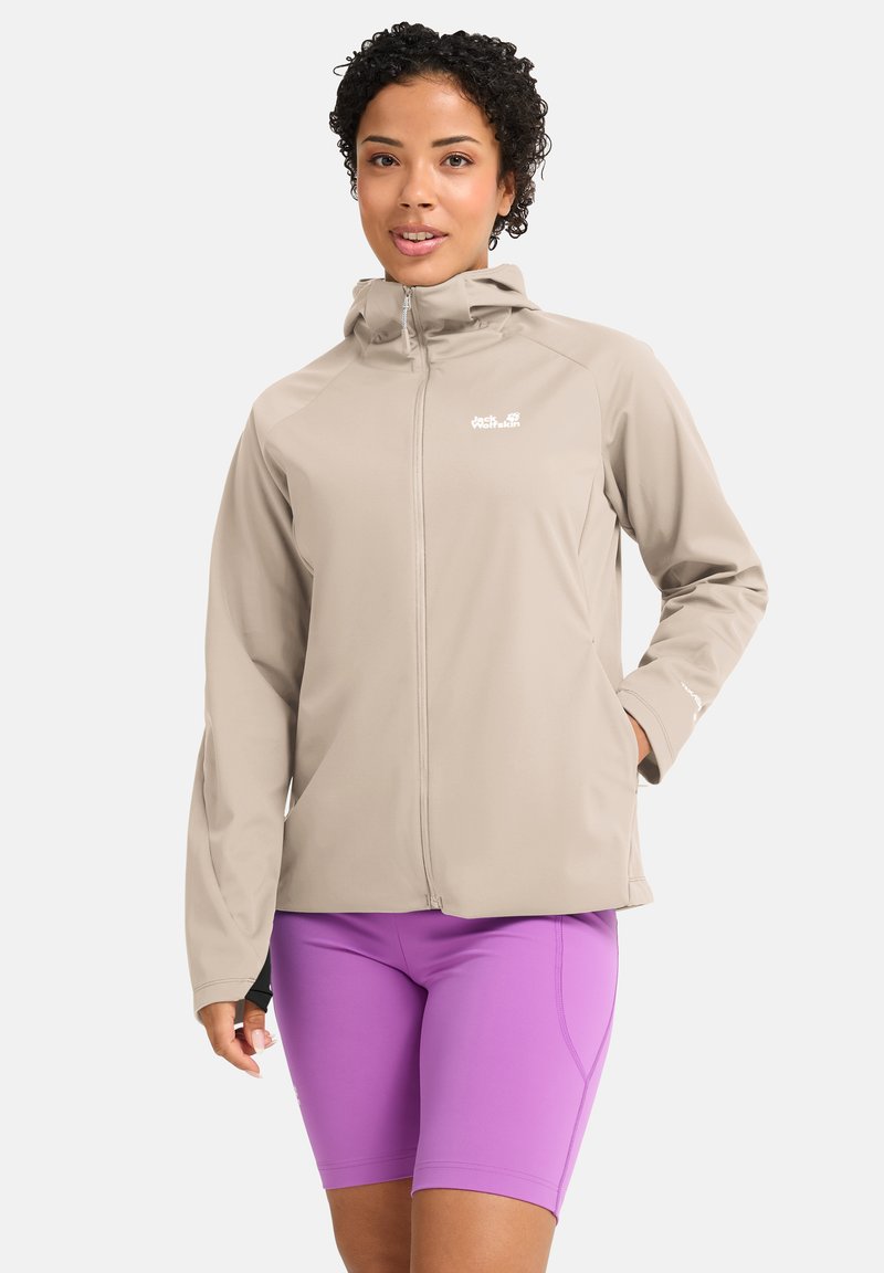 Hellbeige Reißverschlussjacke mit Kapuze aus glattem Stoff. Mit kleinem weißem Logo, elastischen Bündchen und Seitentaschen. Kombiniert mit violetten Shorts.