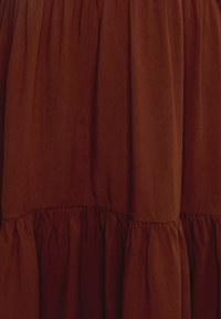 Robe tiered marron en tissu doux, avec une texture froncée à la taille et des détails à volants au bas.