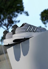 Atletické topánky v bielej a sivej sieťovine s čiernymi akcentmi. Disponujú tromi čiernymi pruhmi, Cloudfoam podrážkou a textúrovaným horným dizajnom.