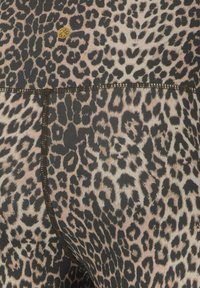 Close-up van een stoffen met luipaardprint, met zwarte en tan vlekken en zichtbare bruine stiksels op een kledingstuk.