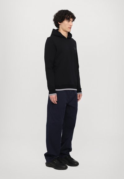 Black hoodie with a front pocket and gray accents, paired with navy blue pants. Worn with black athletic shoes. Model shown from the side.