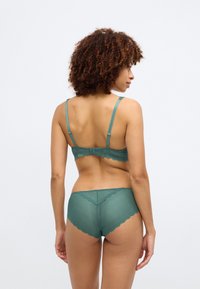 Sutiã teal com acabamento de renda e calcinhas combinando. Tecido suave e texturizado com bordas em formato de escama e alças ajustáveis nas costas.