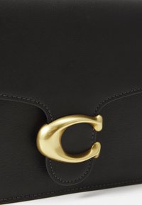 Pochette en cuir noir avec une finition texturée, dotée d'un fermoir ovale doré proéminent et de coutures contrastantes le long des bords.