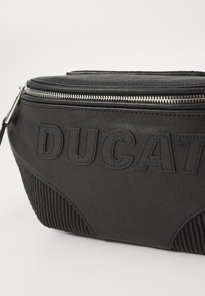 Bolso de cuero negro con una superficie texturizada, que presenta un logo en relieve prominente, cremallera plateada y un diseño acanalado en la parte inferior.
