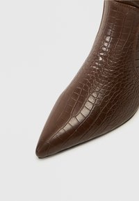 Bottine marron en cuir à texture crocodile, avec un bout pointu et une finition lisse, présentant un discret panneau élastique sur le côté pour un enfilage facile.