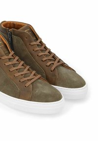 Baskets montantes en suède et cuir vert olive, avec des lacets marron et une semelle en caoutchouc blanche. Détail de fermeture éclair sur le côté.