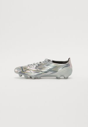 Crampon de football argenté avec finition irisée, dessus texturé, intérieur noir et crampons gris, avec un logo sur la zone des orteils.