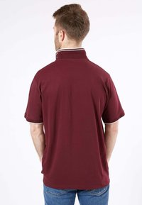 Polo rouge bordeaux avec un col haut, des manches courtes et une bordure d'accent blanche le long du col et des bords des manches. Tissu uni texturé.