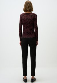 Geribbelde langarmtop in bordeaux met een bloemenpatroon. Gecombineerd met zwarte slim-fit broek en platte zwarte schoenen. Minimale hardwaredetails.