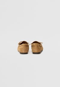 Brown suede loafers with a rounded shape, featuring decorative stitching and a lace accent. Soft texture and low-profile rubber sole.