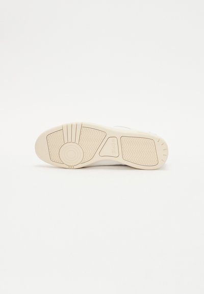 Vit sneakersula med en strukturerad gummiyta, cirkulära och horisontella mönster, samt en logotyp nära hälen.