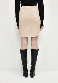Beige kjol med tight passform och slits bak, dragkedjedetalj i midjan, tillsammans med knähöga svarta läderstövlar med klack.