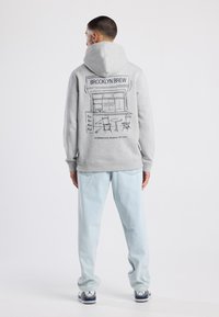 Felpa grigia con stampa grafica di un caffè sulla schiena, abbinata a jeans azzurri chiari e sneakers. Tessuto morbido e vestibilità casual.