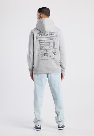 Grijze hoodie met een grafische print van een café op de achterkant, gecombineerd met lichtblauwe jeans en sneakers. Zachte textuur en casual pasvorm.