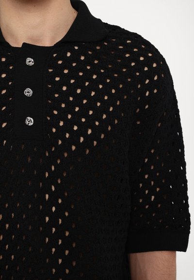 Polo shirt en tricot noir avec un design à mailles ouvertes. Comprend un col et trois boutons décoratifs à l'avant. Manches courtes.