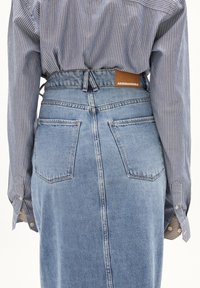 Lichte blauwe spijkerrok met een rechte snit, achterzakken en een logopatch. Gepaard met een blauw-wit gestreept shirt.