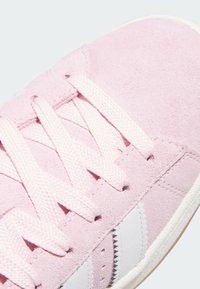 Baskets en daim rose avec des accents en cuir blanc, lacets plats roses et surface texturée. Gros plan sur la partie supérieure et les lacets.