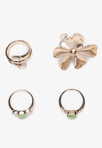 L'ensemble de bijoux dorés comprend une broche florale avec des pétales courbés, deux bagues avec des pierres vertes et transparentes, et une bague en anneau texturée sur le côté.