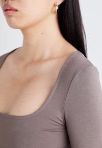 Braunes, tailliertes Oberteil mit U-Ausschnitt und langen Ärmeln, das durch eine glatte, elastische Textur und saubere Nähte besticht.