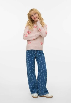 Suéter de punto rosa con patrones florales, combinado con vaqueros de pierna ancha de color azul con un estampado floral. Zapatillas blancas con acentos en beige.