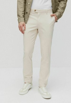 Beige Chinos aus leichtem Stoff mit schmalem Schnitt. Mit einem einzigen Knopfverschluss, Gürtelschlaufen und seitlichen Taschen. Tragen mit weißen Sneakern.