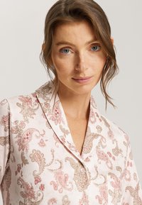 Camisa de pijama rosa claro con intrincados patrones de paisley en rojo y beige. Presenta un diseño con cuello y un cierre de botones en la parte frontal.