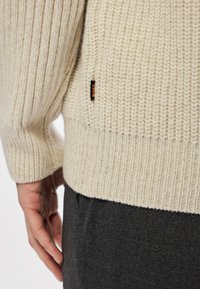 Κρέμ χρώματος πουλόβερ με ραβδωτή υφή και εφαρμοστή στριφώματα. Διαθέτει μια διακριτική ετικέτα λογότυπου στο πλάι. Μαλακό, �πλεκτό ύφασμα.