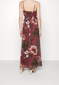 Blommig maxiklänning i vinröd med tunna axelband, smockad midja och en flödande kjol. Har stora, ljusa blommor och gröna blad.