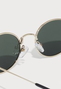 Ringikujulised prillid tumeroheline klaasidega, kuldne metallraam, läbipaistvad nina padjad ja õhuke kuldne vars. Minimalistlik disain koos elegantsete aktsentidega.
