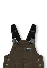 Salopette en coton vert avec des bretelles noires ajustables, des attaches en métal, des poches avant et des boutons-pression verts. Logo Timberland brodé sur la poitrine.