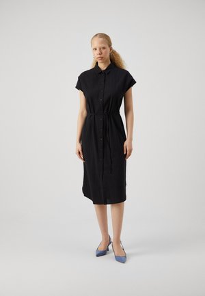 Black, knee-length shirt dress with short sleeves, button closure, and a tie waist. Paired with blue pointed-toe heels. Smooth texture.