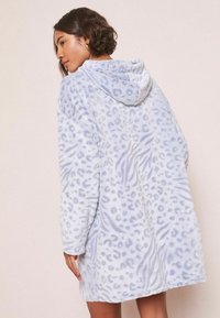 Világoskék kapucnis köpeny, puha, textúrált anyagból, leopárdmintával, sötétebb kék részletekkel és laza szabással.