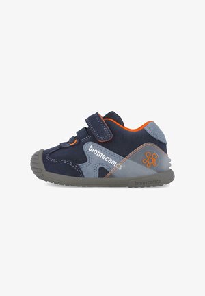 Zapatos de ante azul marino con acentos grises, que presentan una correa de velcro y suela de goma, destacados con detalles y logotipo en naranja.