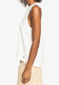 Witte mouwloze top van gestructureerde stof, met een ontspannen pasvorm, ronde halslijn en een klein metalen accent aan de zoom.