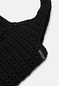 Zwarte geweven tas gemaakt van textuurmateriaal, met een gebogen vorm en een logo-label met "HVISK" dat prominent wordt weergegeven.