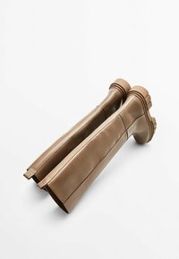 Een paar hoge beige leren laarzen met dikke zolen en zijritsen, plat gelegd op een witte achtergrond.