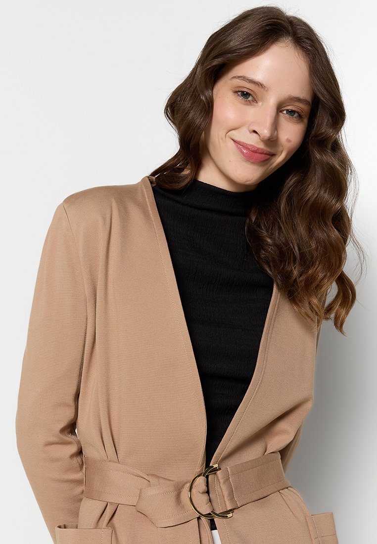 Chaqueta envuelta beige hecha de tejido suave, con una cintura ceñida y un hebilla de metal dorado, parte delantera abierta y mangas largas.