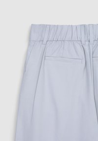 Pantaloni plissettati azzurri chiari con cintura elastica, due tasche laterali e una tasca posteriore singola. Texture liscia e design semplice.