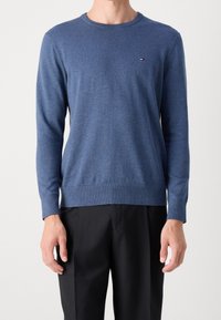 Niebieski sweter z okrągłym dekoltem wykonany z miękkiej dzianiny. Posiada długie rękawy, ściągacze przy mankietach i u dołu, małe logo na piersi oraz dopasowany krój.