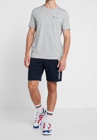 Szara koszulka z krótkim rękawem z małym logo, w połączeniu z granatowymi szortami z białym akcentem. Do tego kolorowe sportowe buty.