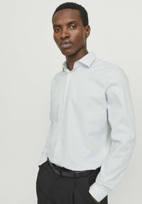 Camicia azzurra chiara a maniche lunghe realizzata in tessuto liscio, con colletto a bottoni e una leggera trama, abbinata a pantaloni neri e una cintura.