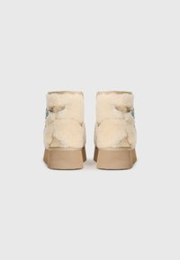 Beige Knöchelstiefel mit Lammfell-Futter und flacher, tanfarbiger Sohle, ausgestattet mit einem strukturierten Obermaterial und dezenten Nahtdetails auf der Rückseite.
