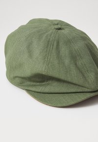 Casquette à motif chevrons verts avec une visière légèrement incurvée, fabriquée en tissu texturé, comportant des coutures brodées et un bouton central sur le dessus.