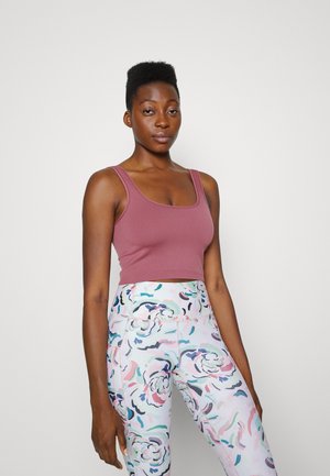 Top cropped em tecido de malha rosa empoeirada, combinado com leggings de cintura alta apresentando um padrão floral colorido em tons pastéis.