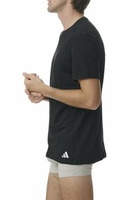 Czarna koszulka z krótkim rękawem, z okrągłym dekoltem, prezentowana na modelu w szarych szortach. Posiada białe logo Adidas na dolnym lewym boku.